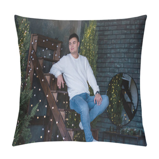 Personality  A Young Man In A White Knitted Sweater, Blue Jeans, Sits On A Wooden Staircase, Smiles Openly At The Camera. Against The Background Of Christmas Trees, Garlands With Lights. Close-up Portrait Of A Guy Resting For The New Year Pillow Covers