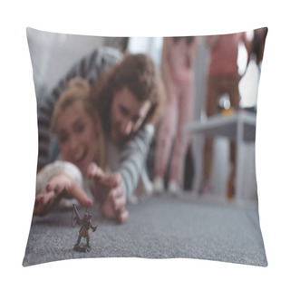Personality  Selective Focus Of Excited Girl And Guy Lying On Floor And Trying To Take Toy Figurine, And Friends Standing On Background Pillow Covers