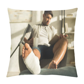 Personality  Selective Focus Of Man With Leg In Plaster Bandage Holding Cup And Reading Book In Armchair  Pillow Covers