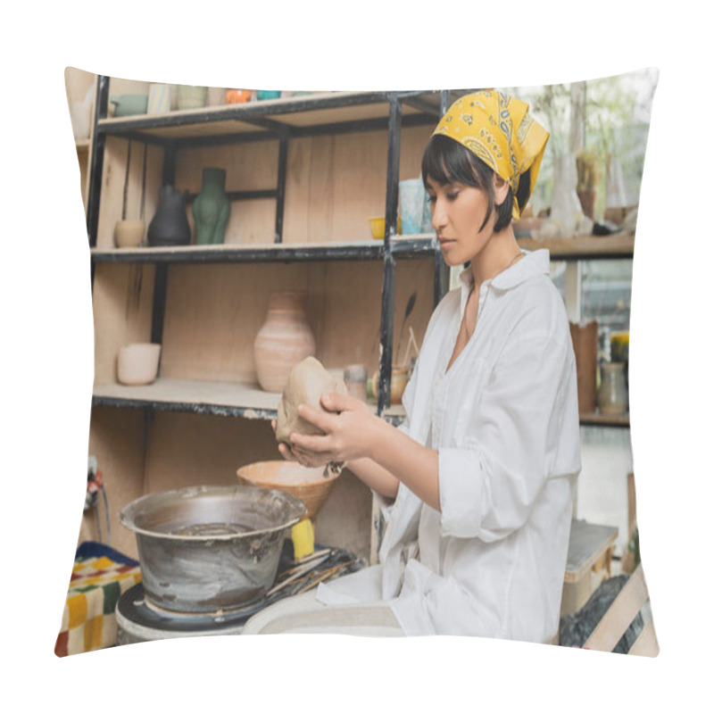 Personality  Young asian female artisan in headscarf and workwear holding clay while working near pottery wheel in ceramic workshop at background, craftsmanship in pottery making pillow covers