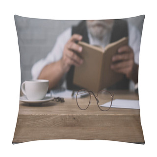 Personality  Senior Man Reading Book At Work Desk With Cup Of Coffee And Eyeglasses On Foreground Pillow Covers