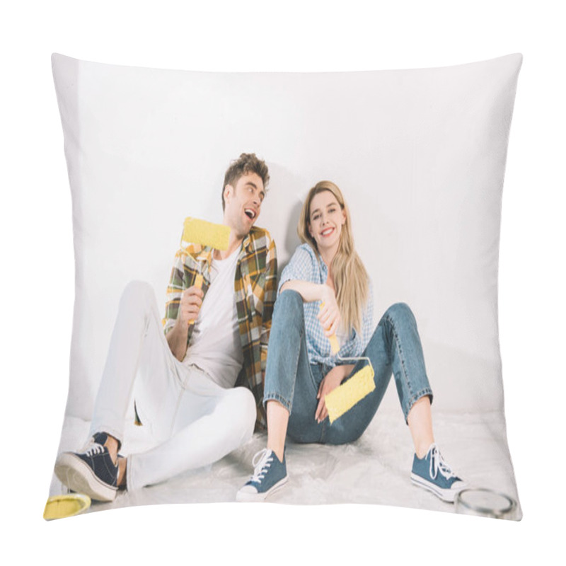 Personality  happy young couple sitting near white wall and holding yellow paint rollers pillow covers