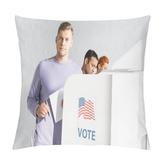 Personality  Man Looking At Camera While Holding Ballot Near Polling Booth With American Flag And Vote Lettering On Blurred Background Pillow Covers