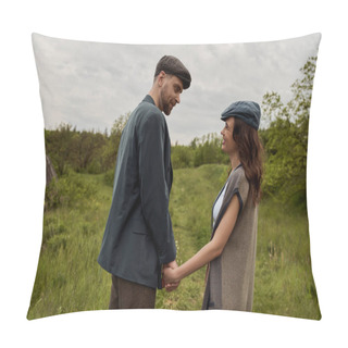 Personality  Bearded And Stylish Man In Jacket And Newsboy Cap Holding Hand And Looking At Cheerful Girlfriend In Vest And Standing Together On Grassy Lawn At Overcast, Stylish Couple In Rural Setting Pillow Covers