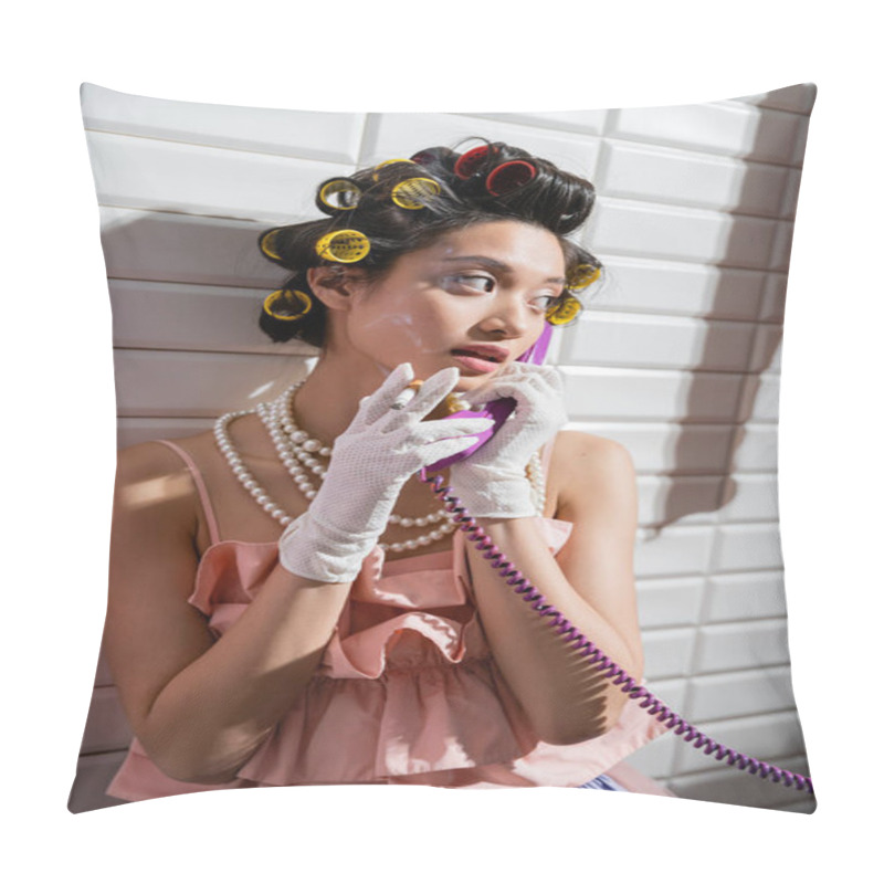 Personality  brunette and asian young woman with hair curlers standing in pink ruffled top, pearl necklace and white gloves, smoking cigarette and talking on retro phone near white tiles, housewife, vintage pillow covers