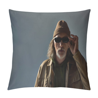 Personality  Fashionable And Hipster Style Senior Man In Beanie Hat And Brown Jacket Adjusting Dark Sunglasses And Looking At Camera On Grey Background, Aging Population Lifestyle Concept Pillow Covers