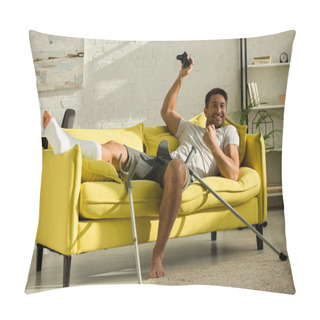 Personality  KYIV, UKRAINE - JANUARY 21, 2020: Exited Man With Broken Leg Holding Joystick And Showing Win Gesture On Couch At Home Pillow Covers