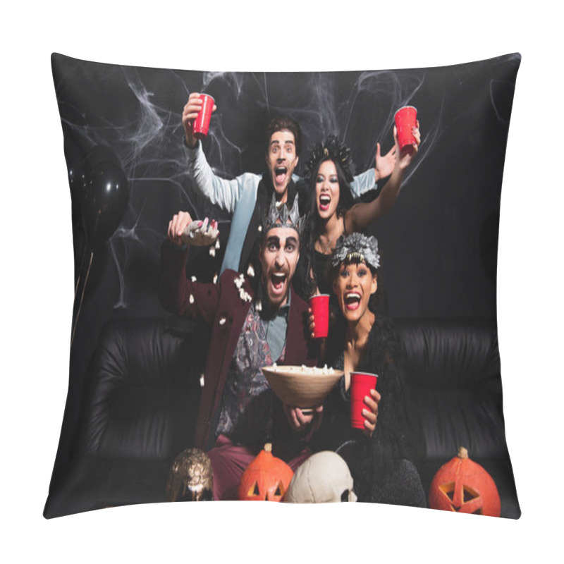 Personality  thrilled multicultural friends in halloween costumes near popcorn, carved pumpkins and skulls on black pillow covers