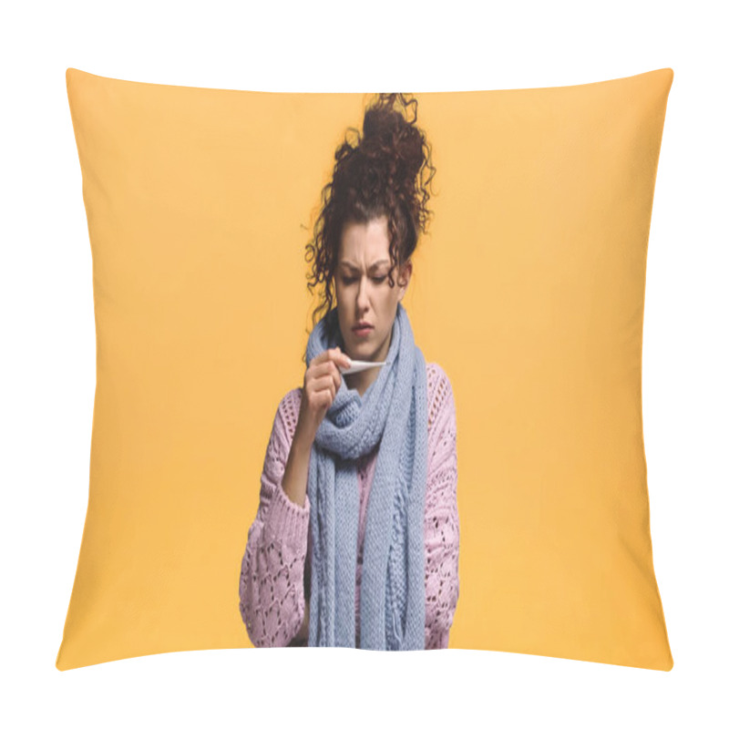 Personality  displeased woman in knitted sweater and scarf looking at thermometer isolated on orange pillow covers