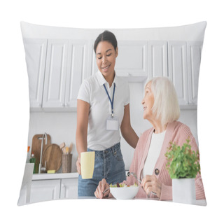 Personality  Happy Multiracial Social Worker Holding Cup Of Tea Near Retired Woman With Grey Hair Having Lunch In Kitchen  Pillow Covers