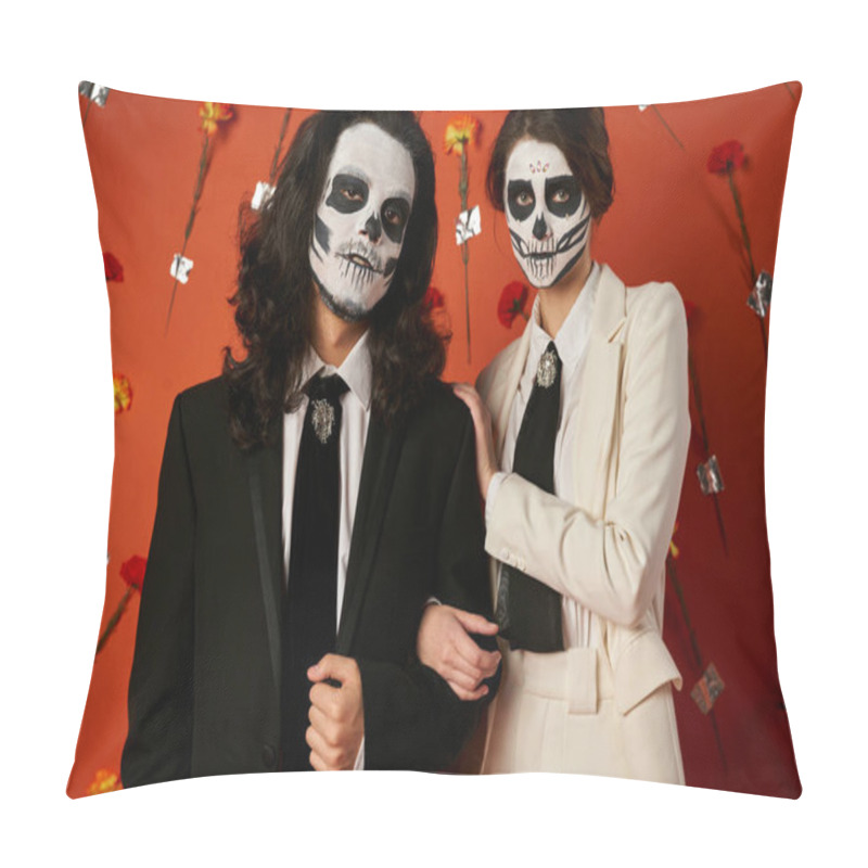 Personality  couple in eerie sugar skull makeup and festive attire looking at camera on red backdrop with flowers pillow covers