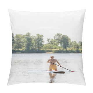 Personality  Young And Active Man In Yellow Swim Shorts Holding Paddle And Kneeling On Sup Board While Sailing On Scenic River With Green Trees On Bank With Picturesque Riverside On Background Pillow Covers
