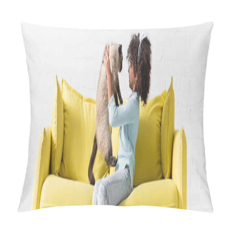 Personality  Side view of curly african american girl holding and looking at siamese cat, while sitting on sofa at home, banner pillow covers