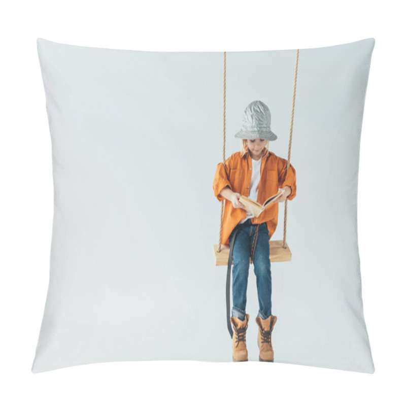Personality  cute kid in jeans and orange shirt sitting on swing and reading book on grey background pillow covers