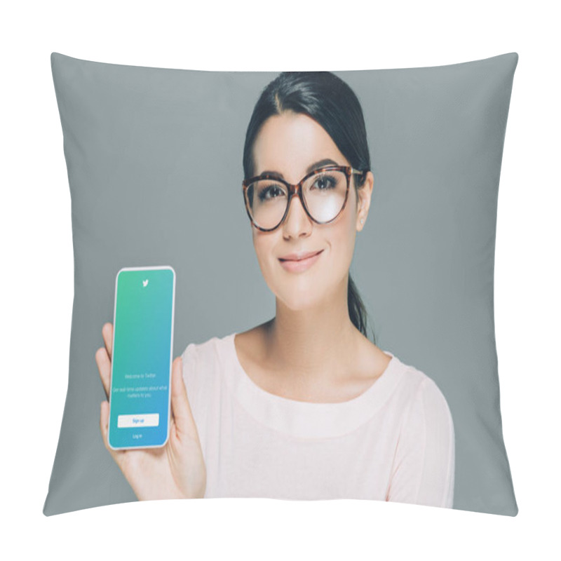 Personality  portrait of smiling woman in eyeglasses showing smartphone with twitter app on screen isolated on grey pillow covers