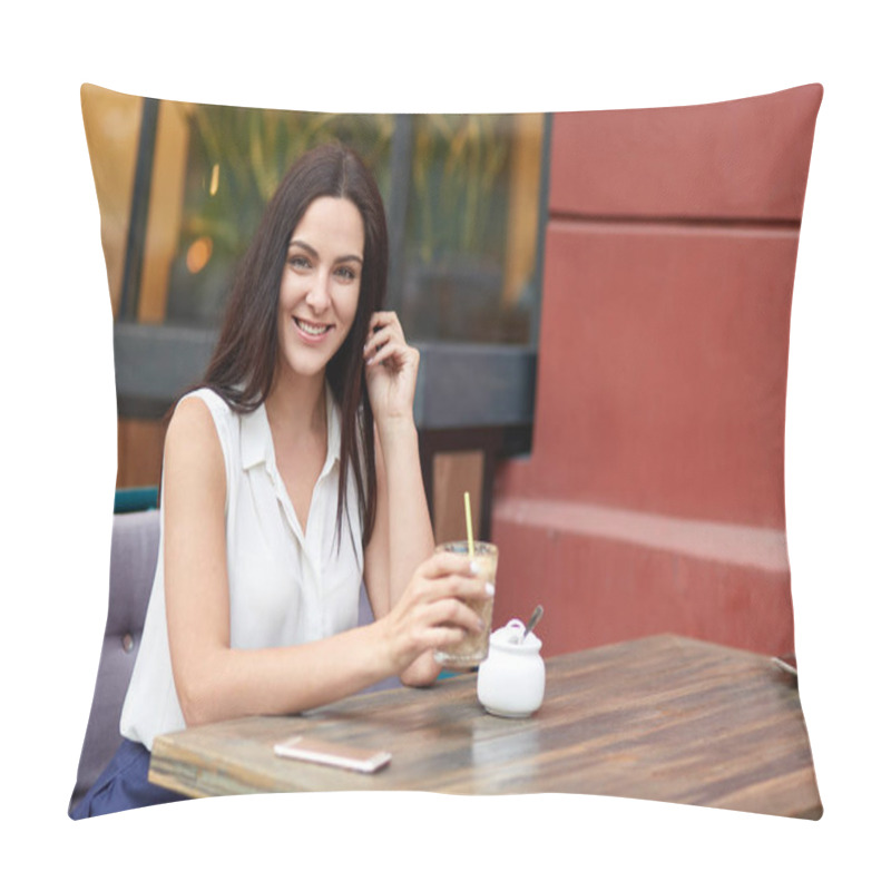 Personality  Cheerful European woman enjoys leisure time, drinks milk shake at outdoor cafeteria, spends weekened in big city, waits for call on smart phone, looks positively, dressed in white stylish blouse pillow covers
