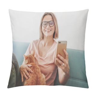 Personality  Pretty Happy Mature Woman In Glasses Sits On A Blue Sofa With A Domestic Red Cat On Her Lap And A Smartphone In Her Hands. Online Shopping And Online News While Sitting At Home Pillow Covers
