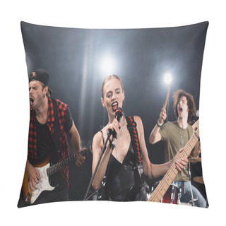 Personality  KYIV, UKRAINE - AUGUST 25, 2020: Blonde Vocalist With Electric Guitar Singing In Microphone Near Guitarist And Drummer With Backlit On Blurred Background Pillow Covers