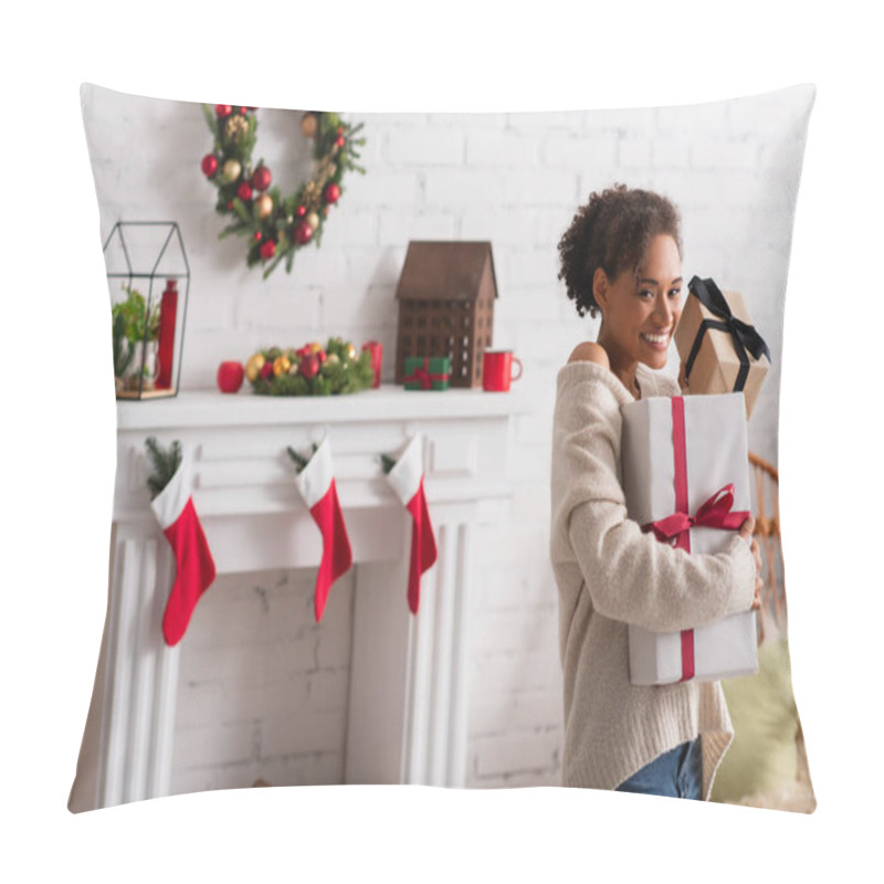 Personality  Cheerful african american woman holding christmas presents near blurred fireplace at home  pillow covers