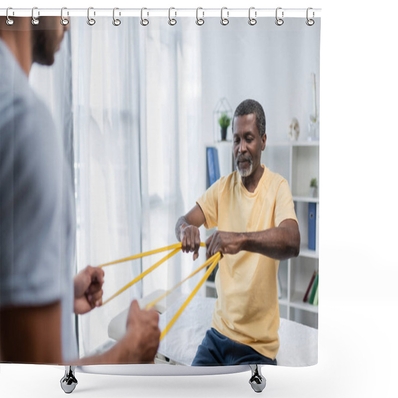 Personality  blurred rehabilitologist and african american patient doing exercise with elastics shower curtains