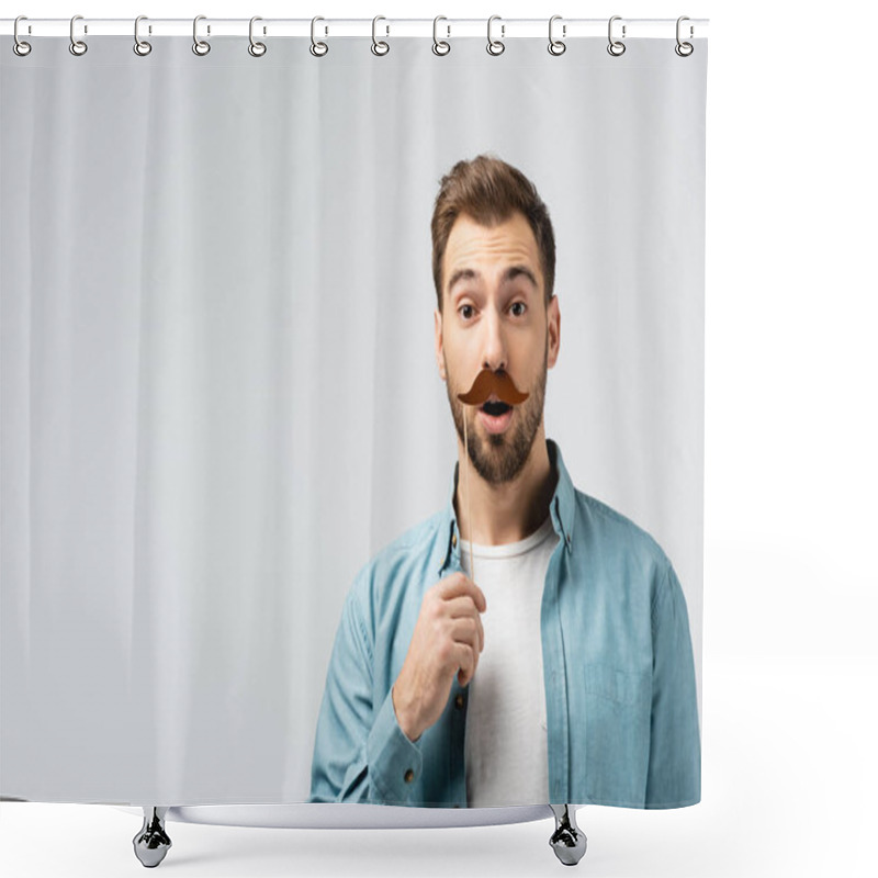 Personality  shocked young man with fake mustache on stick isolated on grey shower curtains