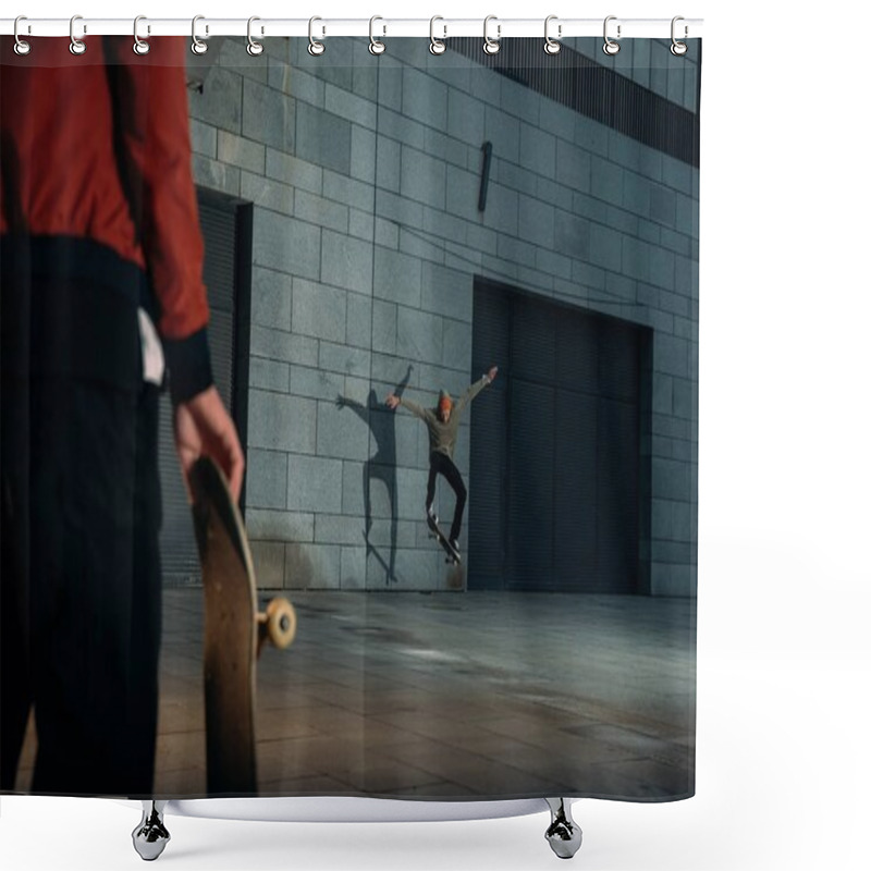 Personality  cropped shot of man standing with skateboard while his partner doing trick on background shower curtains