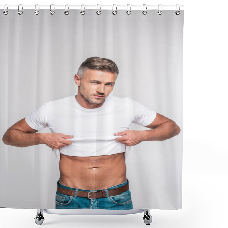 Personality  handsome man in jeans taking off white t-shirt and looking at camera isolated on grey shower curtains
