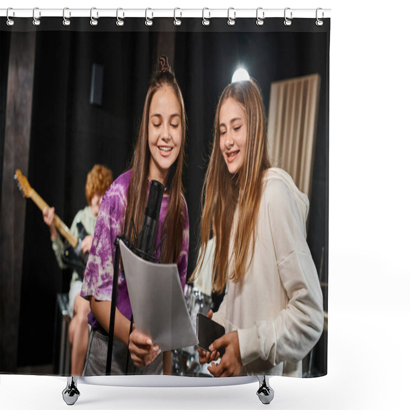 Personality  focus on joyful teenage girls singing and looking at lyrics with blurred guitarist boy on backdrop shower curtains