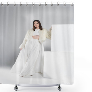 Personality  Full Length Of Young Woman In Faux Fur Jacket And Total White Outfit Leaning On Cubes While Posing On Grey Shower Curtains