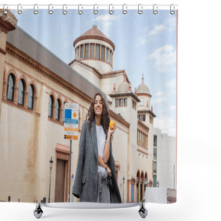 Personality  Cheerful Young And Curly Woman In Casual Warm Jacket Holding Ripe Orange And Leash While Looking At Camera Near Blurred Historical Landmark On Urban Street In Barcelona, Spain, Ancient Building Shower Curtains