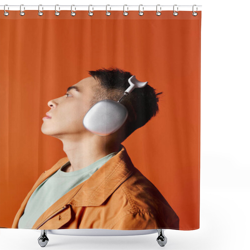 Personality  A handsome Asian man in stylish attire listening to music with headphones on his ears against an orange studio background. shower curtains