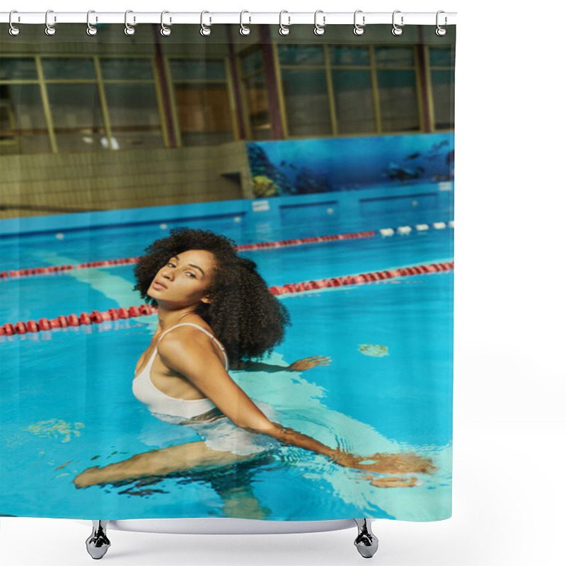 Personality  young and curly african american woman in bathing suit standing by pool ladder with blue water shower curtains