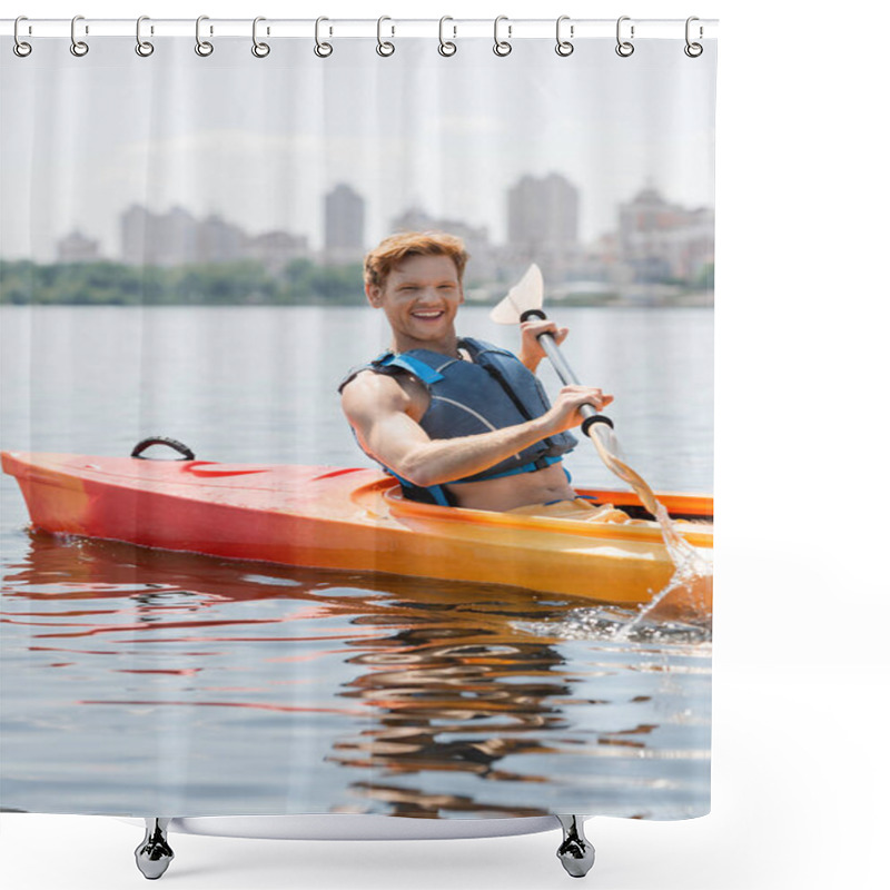 Personality  Young And Overjoyed Redhead Man In Life Vest Looking At Camera And Holding Paddle While Sailing In Sportive Kayak On Lake With Cityscape On Blurred Background Shower Curtains