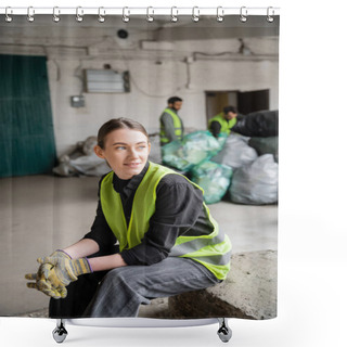 Personality  Positive Young Sorter In High Visibility Vest And Gloves Looking Away While Relaxing Near Blurred Colleagues And Plastic Bags At Background In Garbage Sorting Center, Recycling Concept Shower Curtains
