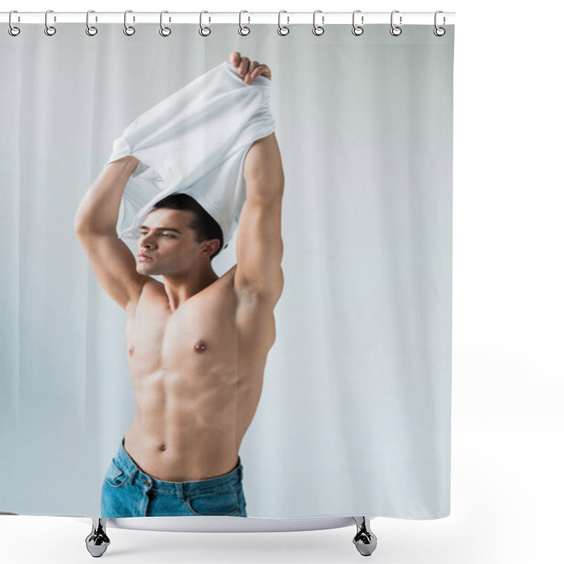 Personality  muscular and handsome man taking off white t-shirt while standing on white  shower curtains