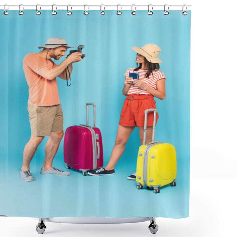 Personality  Happy Man In Hat Taking Photo Of Girl With Passports While Holding Vintage Camera And Standing Near Luggage On Blue Shower Curtains