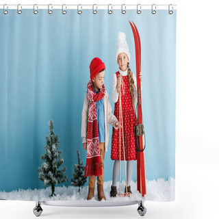 Personality  Kid In Hat And Scarf Pointing With Finger Near Sister Holding Ski Poles And Skis While Standing On Blue Shower Curtains