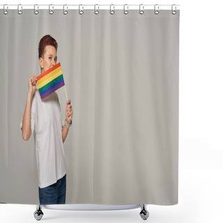 Personality  Redhead Queer Model In White T-shirt Posing With Small LGBT Flat Near Face Looking At Camera On Grey Shower Curtains