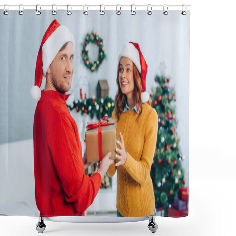 Personality  smiling man in santa hat looking at camera while presenting gift box to excited wife shower curtains