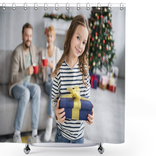 Personality  Cheerful Girl Holding Christmas Gift And Looking At Camera Near Blurred Mother And Dad At Home  Shower Curtains